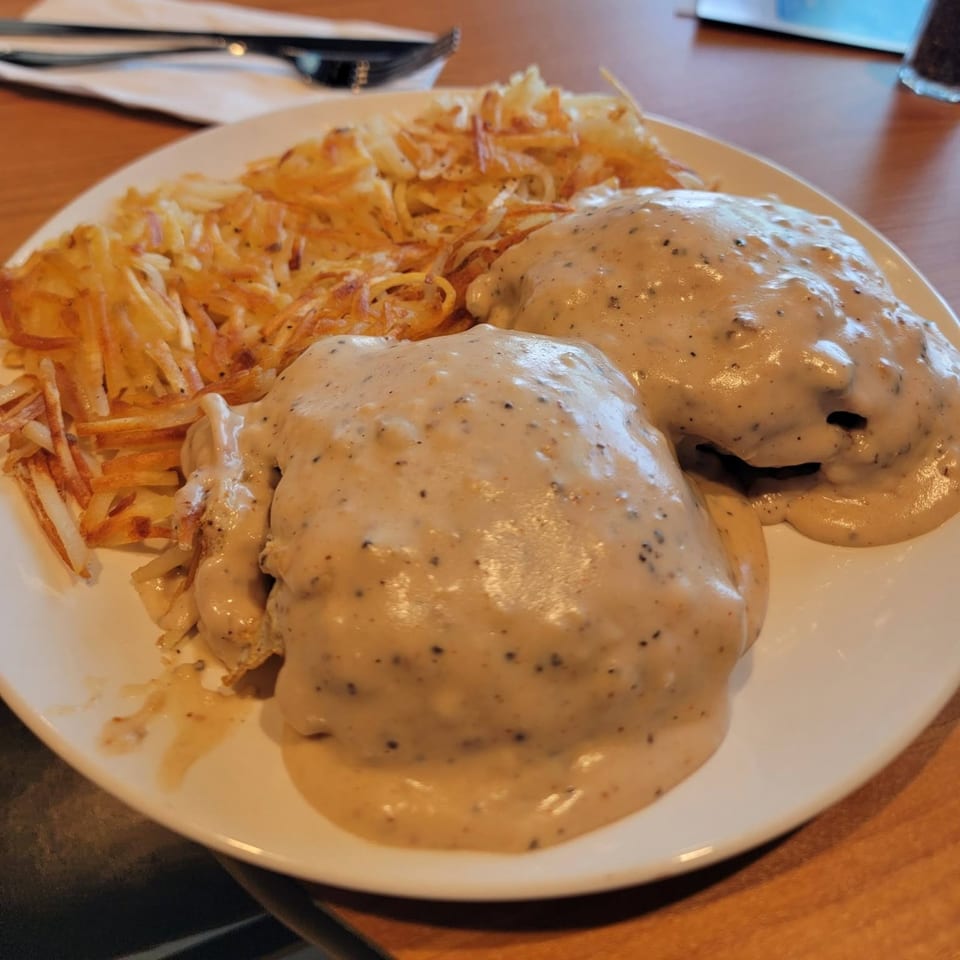 Biscuits and gravy with a side of hash browns on a white plate.