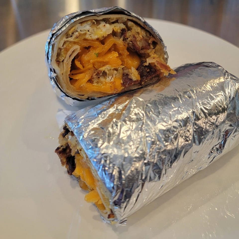 A breakfast burrito, cut in half, revealing eggs, cheese, and meat, wrapped in foil.