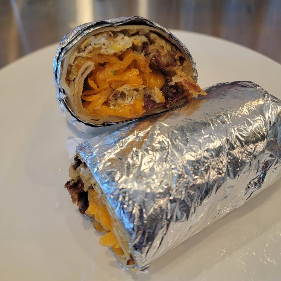 A breakfast burrito, cut in half and wrapped in foil, reveals eggs, cheese, and meat.