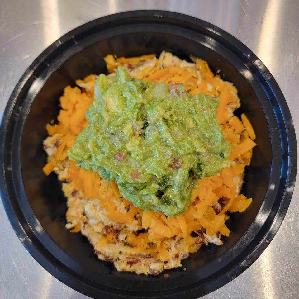 A black bowl filled with scrambled eggs, shredded cheese, and a dollop of guacamole.