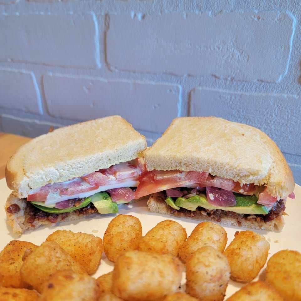 A sandwich cut in half with avocado, tomato, and red onion, served with tater tots.